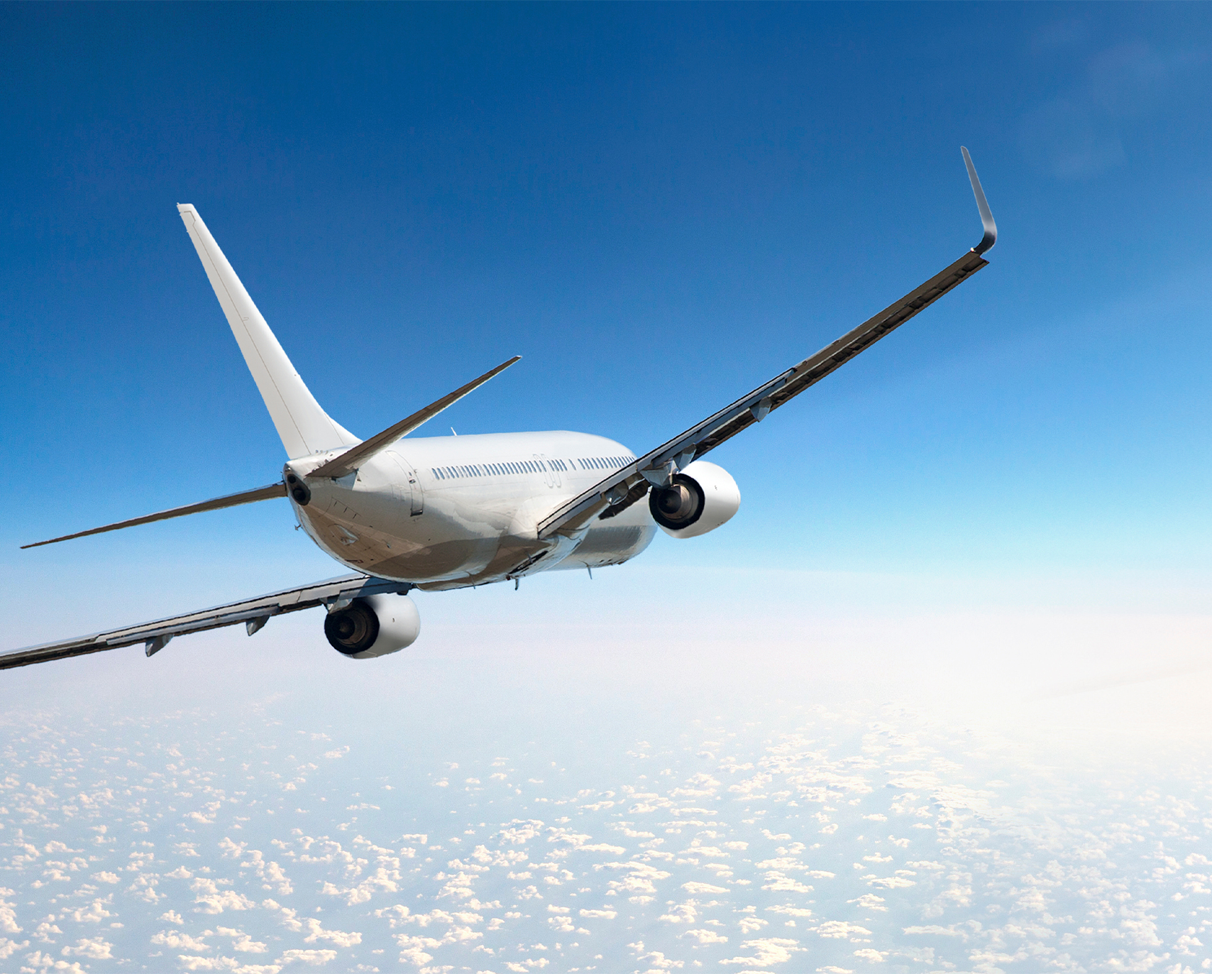 Ein großes Flugzeug fliegt hoch am Himmel, umgeben von blauen Wolken und strahlendem Sonnenlicht.